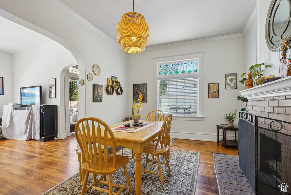 Dining room with arched walkways, wood finished floors, a brick fireplace, ornamental molding, and baseboards