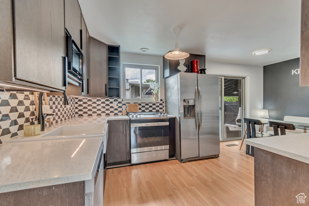 Kitchen featuring stainless steel appliances, backsplash, open shelves, and light wood finished floors