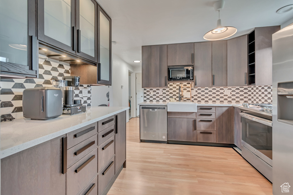 Kitchen with appliances with stainless steel finishes, a sink, decorative backsplash, light wood-type flooring, and light stone countertops