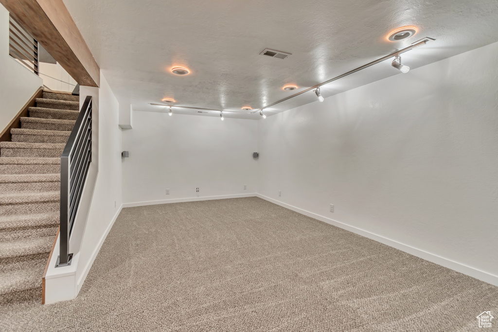 Finished basement with carpet floors, track lighting, stairs, and baseboards