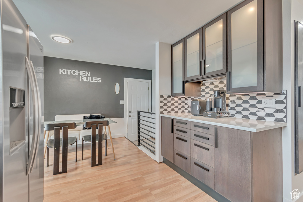 Kitchen featuring stainless steel fridge with ice dispenser, light countertops, tasteful backsplash, light wood finished floors, and glass insert cabinets