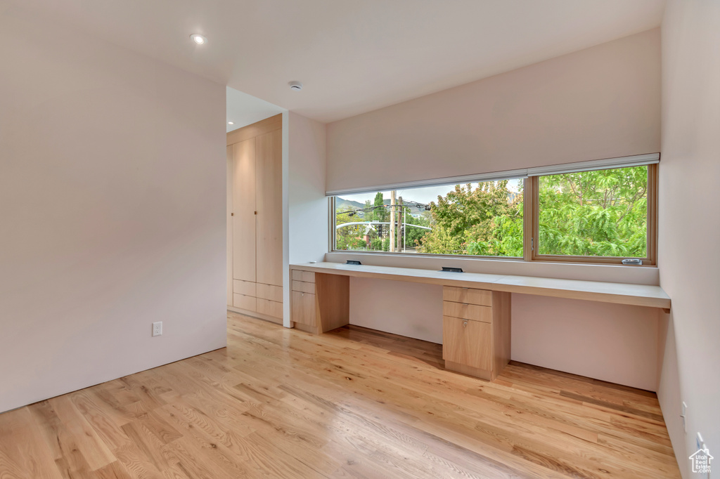 Unfurnished office with built in desk, plenty of natural light, light wood finished floors, and recessed lighting