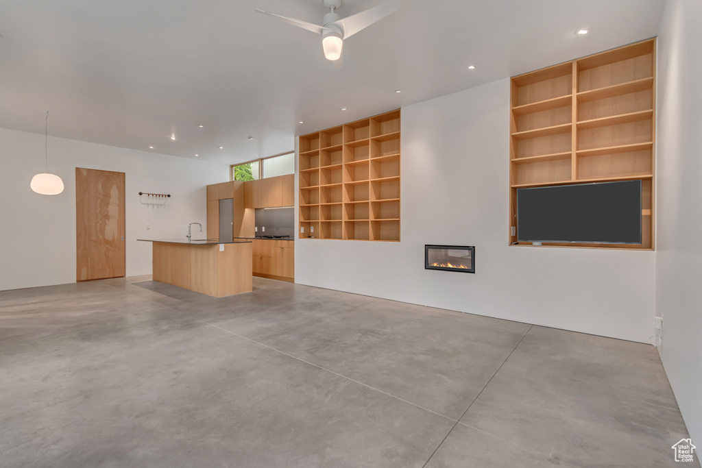 Unfurnished living room with concrete floors, built in features, a glass covered fireplace, a sink, and ceiling fan