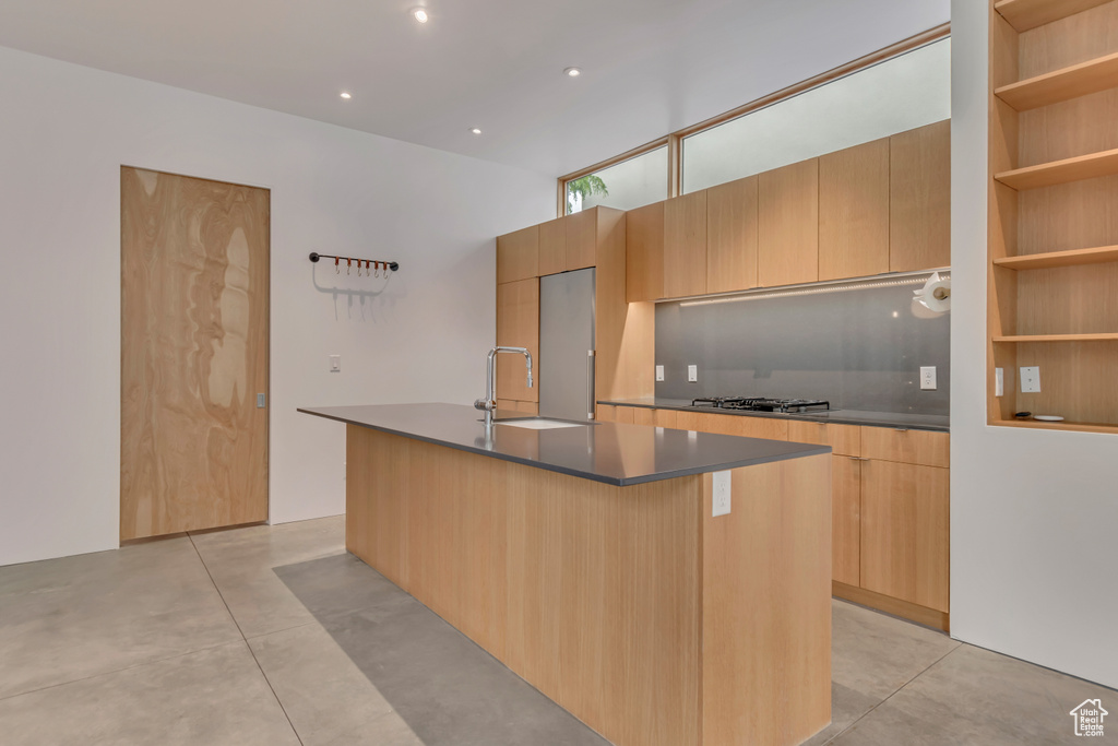 Kitchen featuring modern cabinets, finished concrete floors, a kitchen island with sink, dark countertops, and a sink