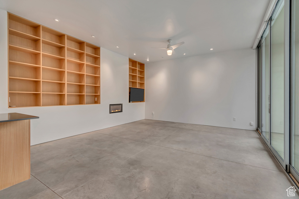 Unfurnished room featuring concrete floors, built in features, ceiling fan, a glass covered fireplace, and recessed lighting