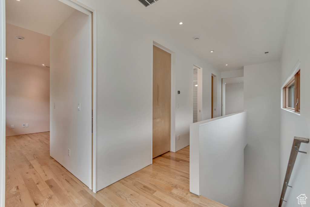 Corridor with an upstairs landing, light wood finished floors, and recessed lighting