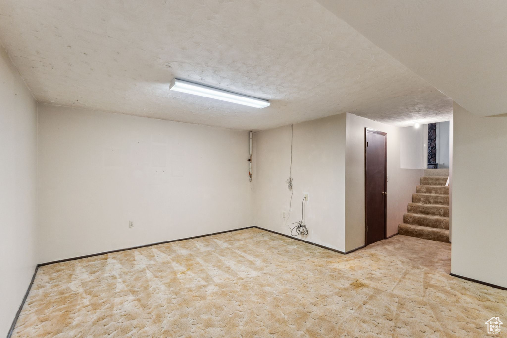 Finished basement with light colored carpet, a textured ceiling, stairway, and baseboards