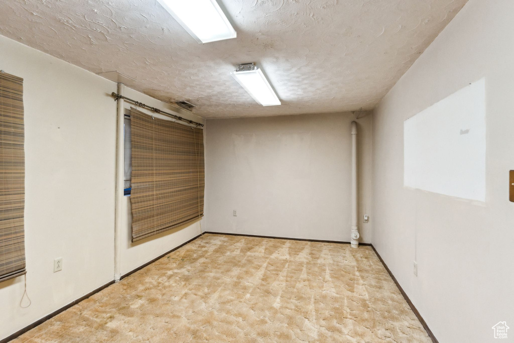Empty room with a textured ceiling, light carpet, and baseboards