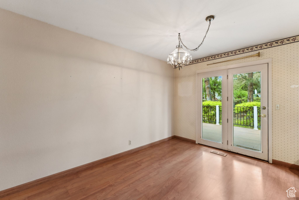 Unfurnished room featuring wood finished floors, a chandelier, baseboards, and wallpapered walls