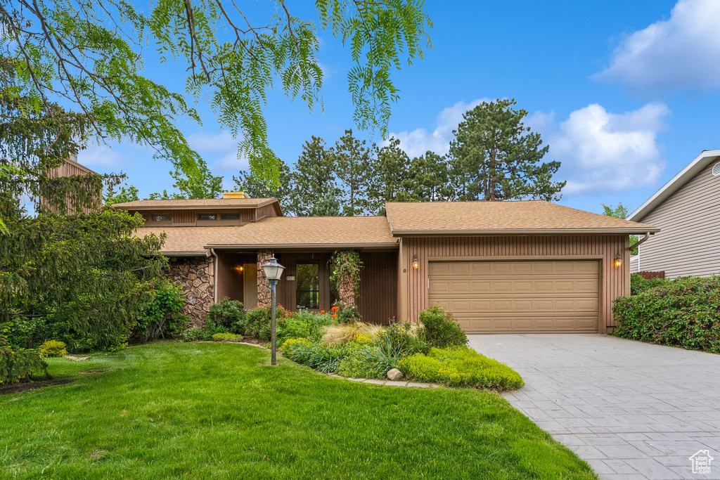 View of front of house featuring a garage, a front yard, stone siding, and driveway