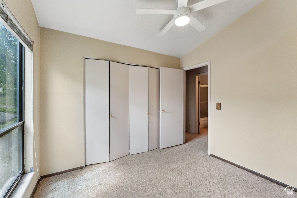 Unfurnished bedroom featuring light colored carpet, lofted ceiling, a closet, and a ceiling fan