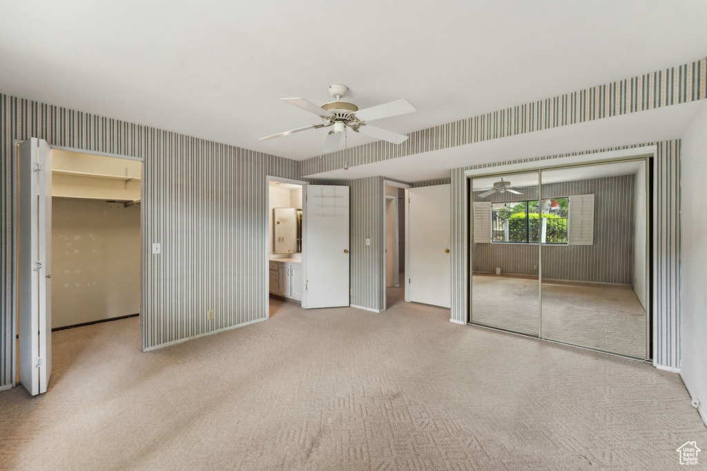 Unfurnished bedroom with a closet, carpet flooring, wallpapered walls, a walk in closet, and connected bathroom