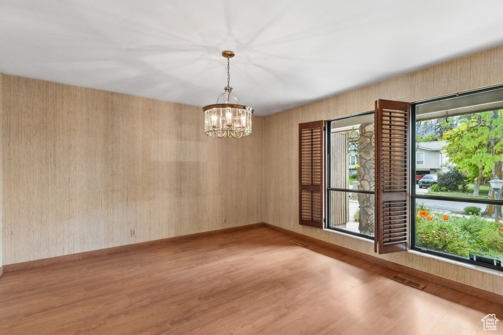 Empty room featuring a chandelier, wood finished floors, and baseboards