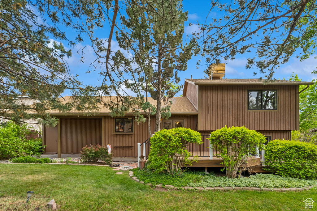 Back of property with a yard, a chimney, a deck, and a shingled roof