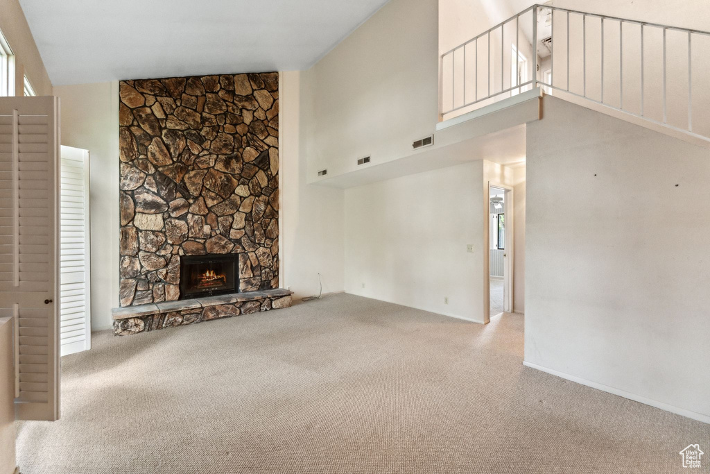 Unfurnished living room with carpet floors, high vaulted ceiling, and a stone fireplace