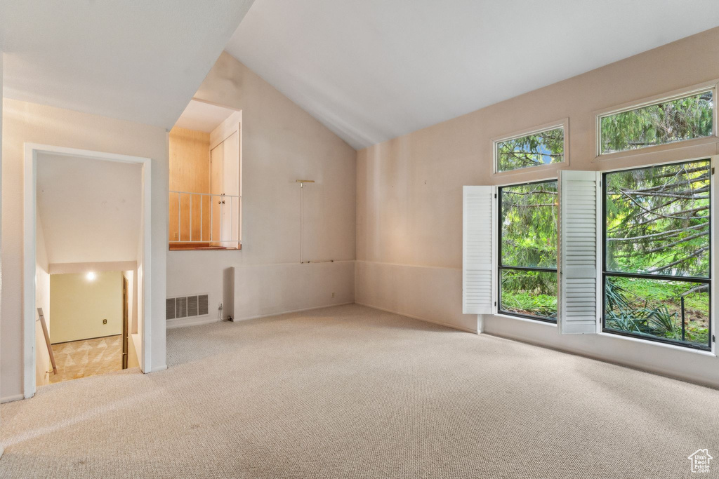 Carpeted spare room featuring vaulted ceiling
