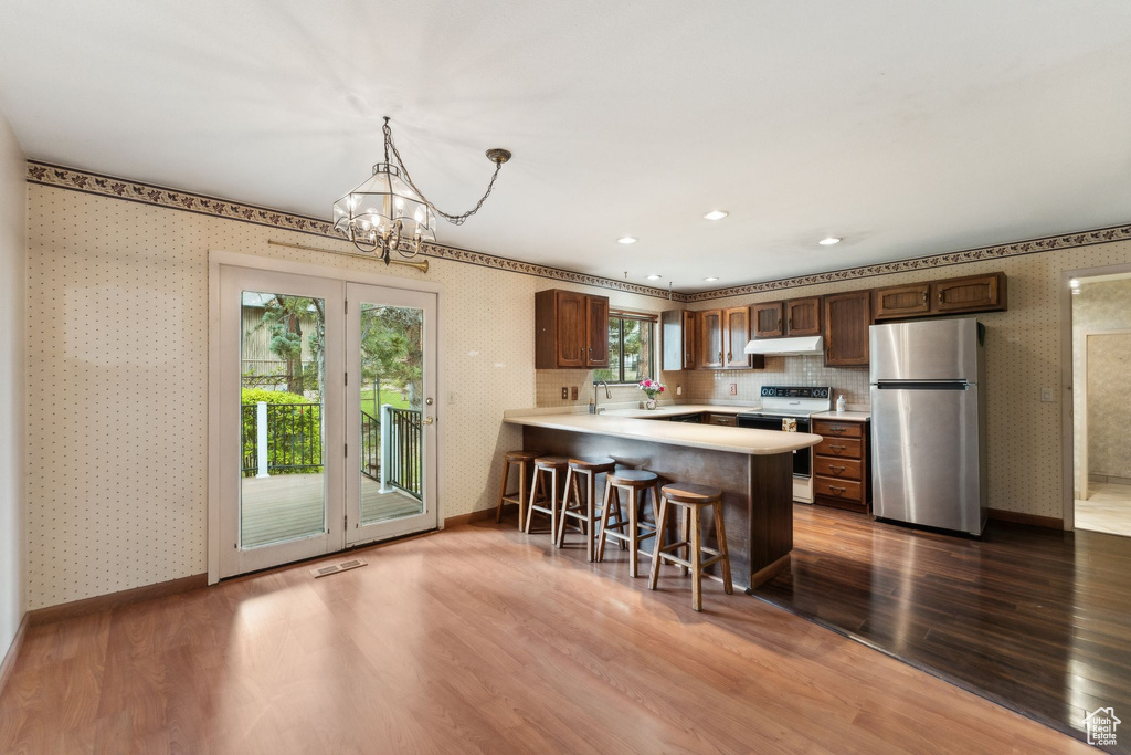 Kitchen featuring freestanding refrigerator, electric stove, wallpapered walls, under cabinet range hood, and light countertops