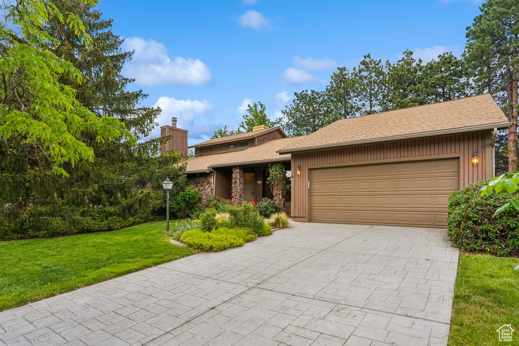 View of front of home with an attached garage, a chimney, decorative driveway, and a front lawn