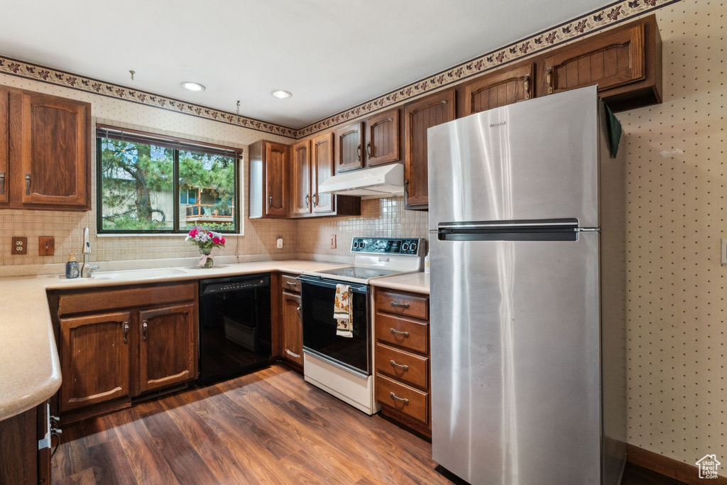 Kitchen with freestanding refrigerator, range with electric cooktop, dishwasher, under cabinet range hood, and light countertops