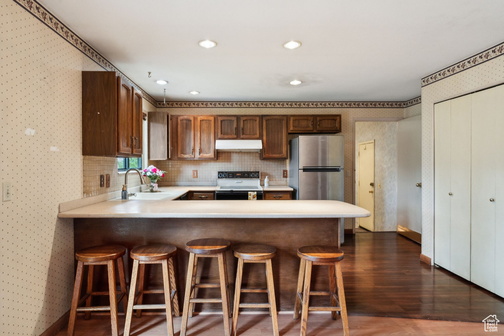 Kitchen with a sink, electric range, freestanding refrigerator, under cabinet range hood, and light countertops