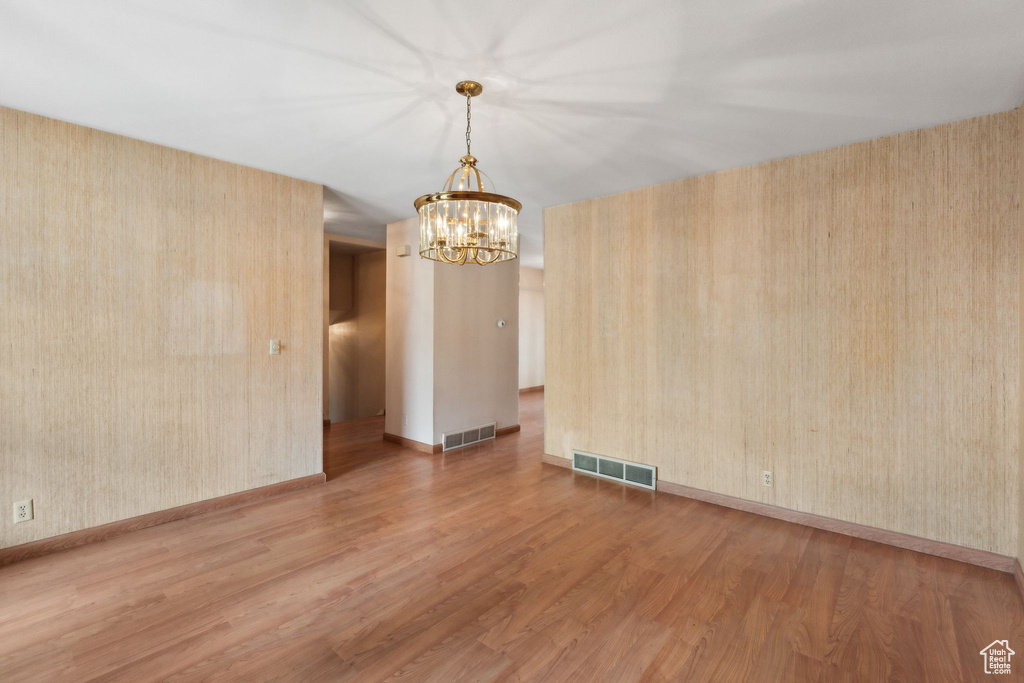 Unfurnished room featuring a chandelier, wood finished floors, and baseboards