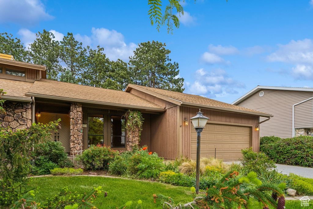 View of front of home with a garage, driveway, stone siding, a front yard, and a shingled roof