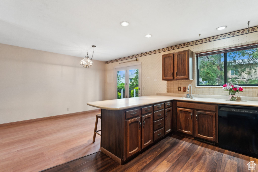 Kitchen featuring dishwasher, a sink, a peninsula, light countertops, and dark wood finished floors