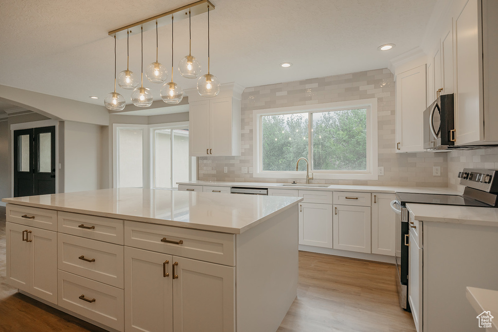 Kitchen with appliances with stainless steel finishes, a sink, a kitchen island, decorative backsplash, and light wood finished floors