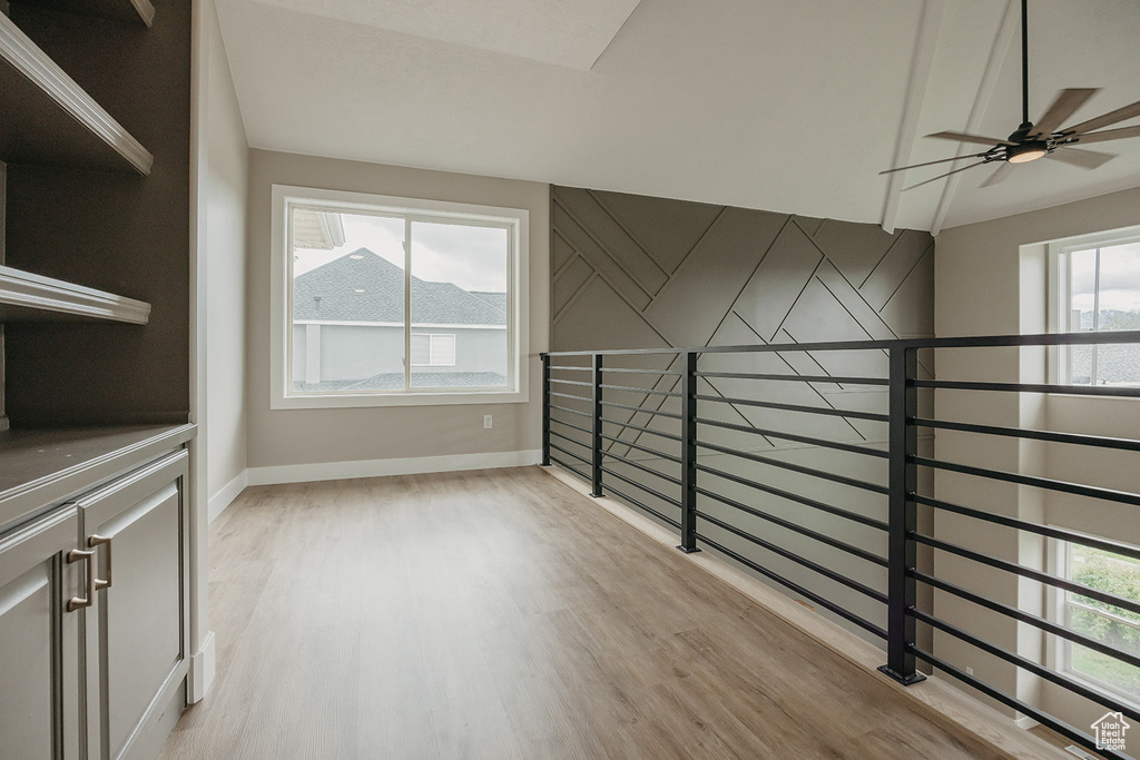 Spare room featuring baseboards, light wood-type flooring, ceiling fan, and lofted ceiling