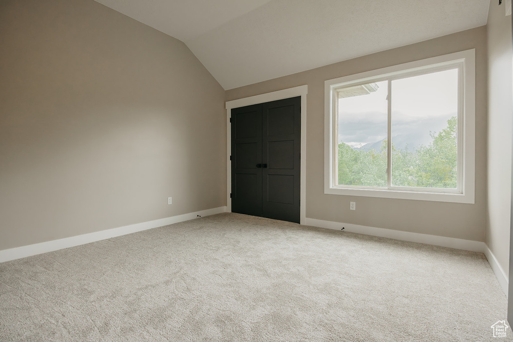 Carpeted spare room featuring baseboards and vaulted ceiling