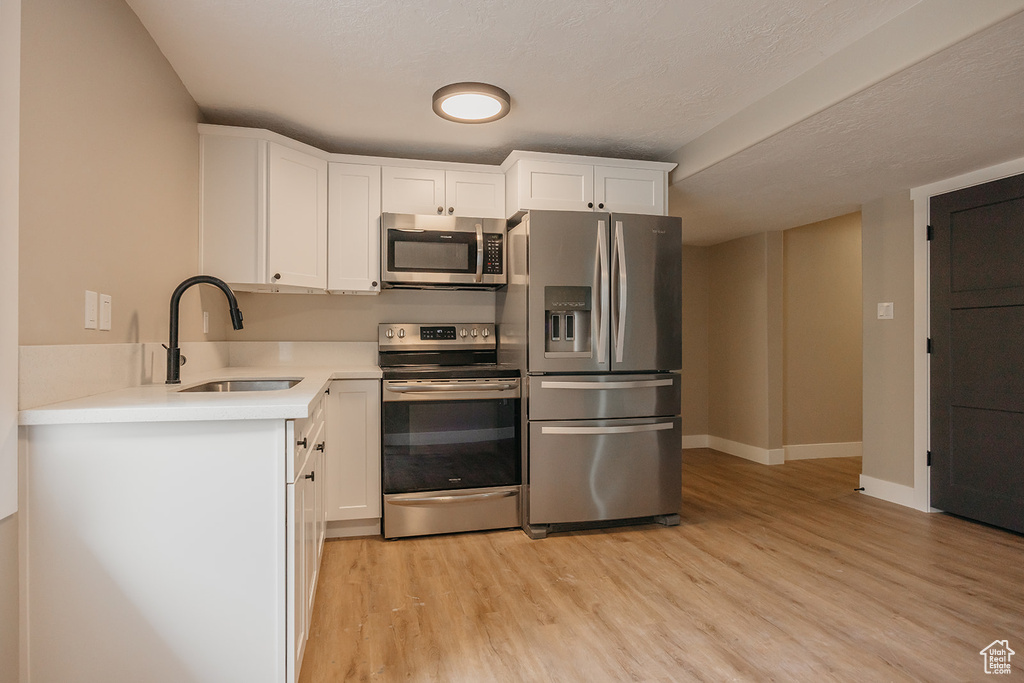 Kitchen featuring stainless steel appliances, a sink, light wood-type flooring, and white cabinets