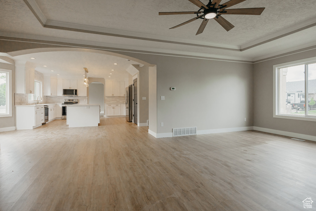 Unfurnished living room with a tray ceiling, healthy amount of natural light, ceiling fan, arched walkways, and ornamental molding