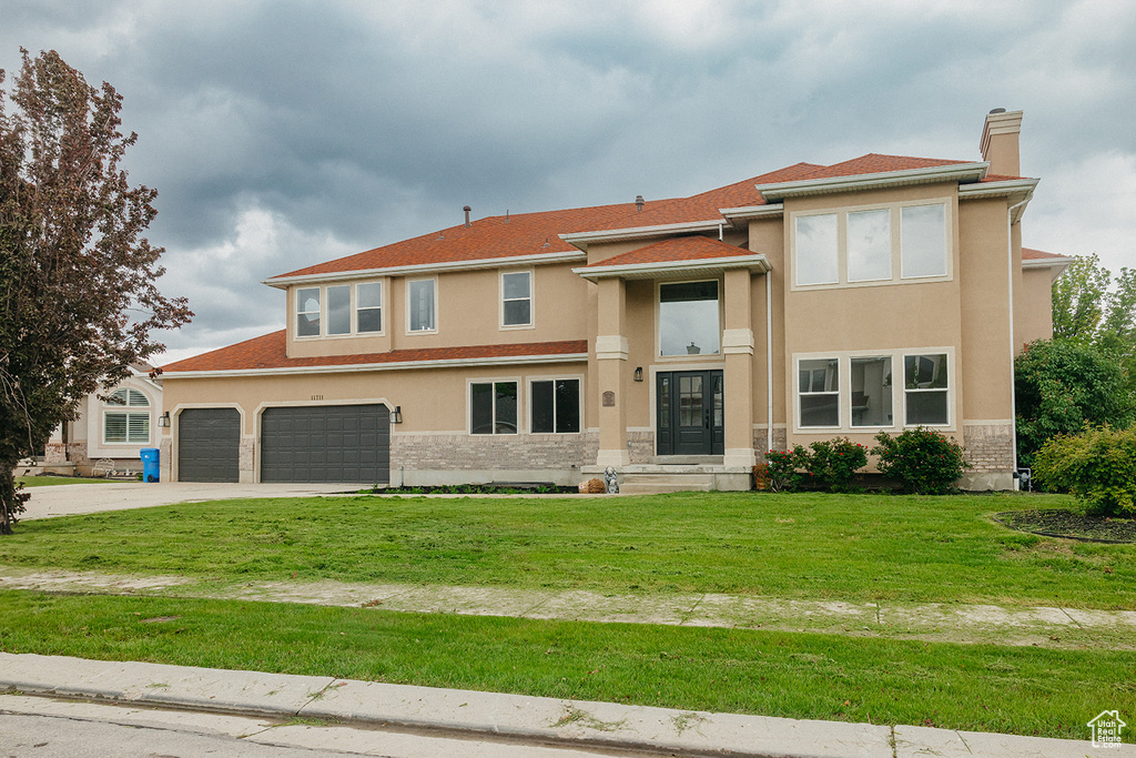 View of front facade featuring a chimney, driveway, stucco siding, and a front lawn