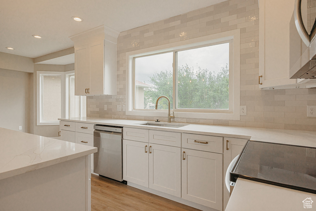 Kitchen featuring stainless steel appliances, a sink, white cabinets, light wood-style floors, and decorative backsplash