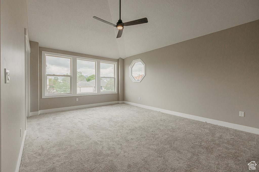 Spare room with ceiling fan, carpet, baseboards, vaulted ceiling, and a textured ceiling