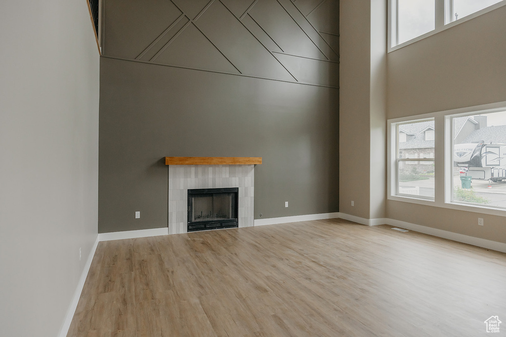 Unfurnished living room with wood finished floors, a tiled fireplace, a high ceiling, and baseboards