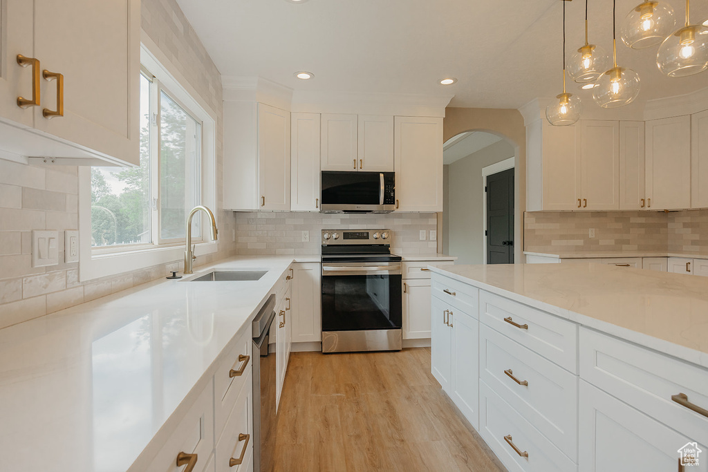 Kitchen with appliances with stainless steel finishes, a sink, white cabinets, backsplash, and arched walkways