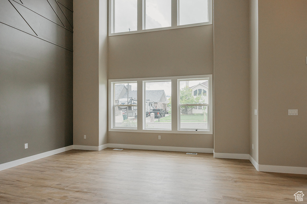 Spare room featuring plenty of natural light, a towering ceiling, light wood-style flooring, and baseboards