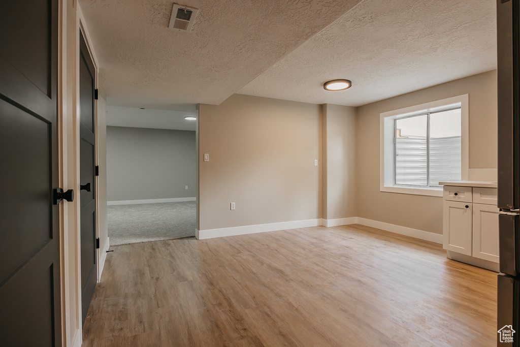 Unfurnished room featuring light wood-type flooring, baseboards, and a textured ceiling