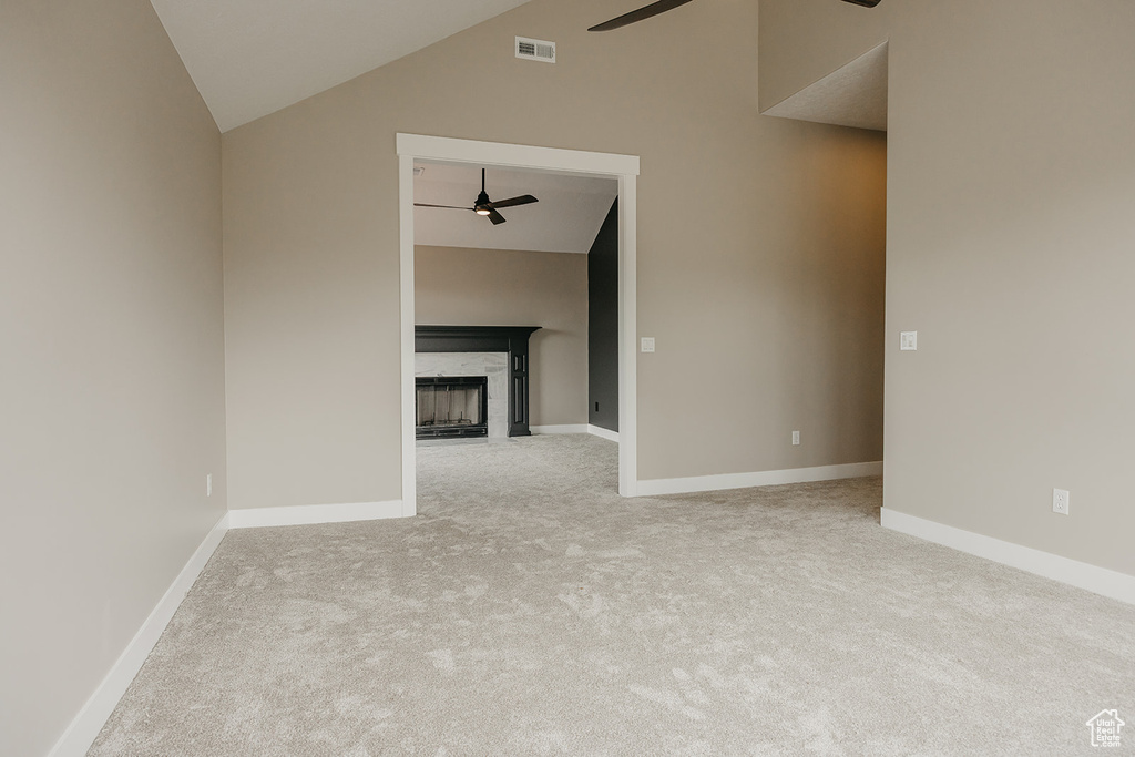 Unfurnished living room with a ceiling fan, carpet, high vaulted ceiling, a tiled fireplace, and baseboards