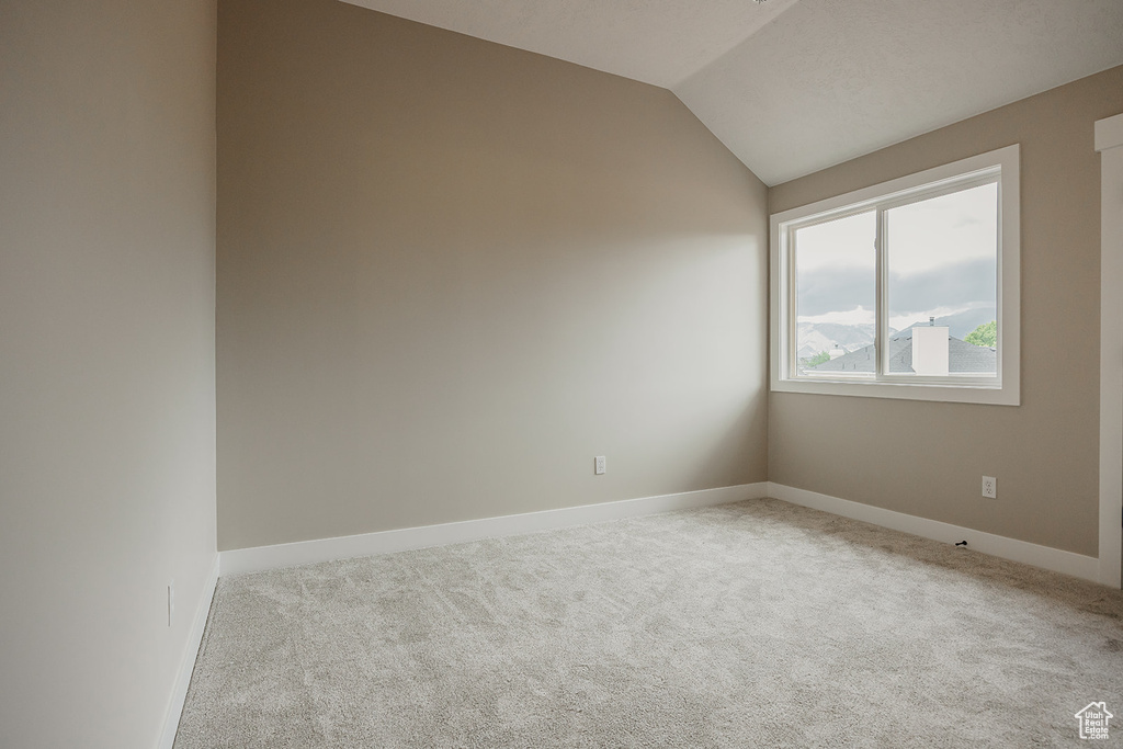 Empty room featuring carpet floors, vaulted ceiling, and baseboards