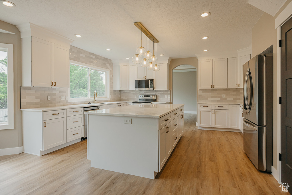Kitchen with appliances with stainless steel finishes, arched walkways, light wood-style floors, a sink, and white cabinets