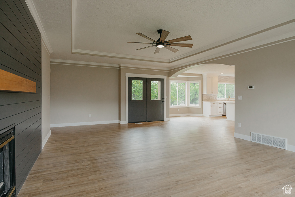Unfurnished living room with arched walkways, ornamental molding, a ceiling fan, a tray ceiling, and a fireplace