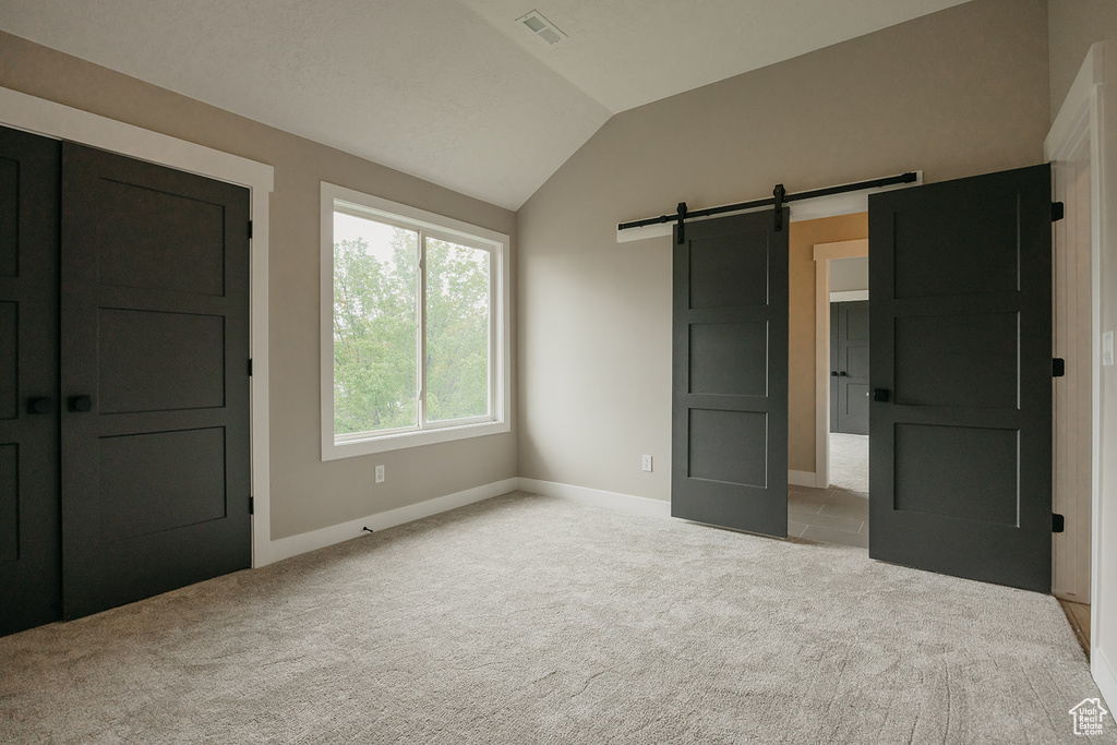 Unfurnished bedroom with vaulted ceiling, carpet floors, a barn door, and baseboards
