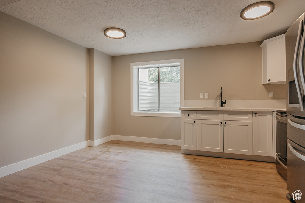 Kitchen with a sink, light wood-style floors, light countertops, white cabinets, and a textured ceiling