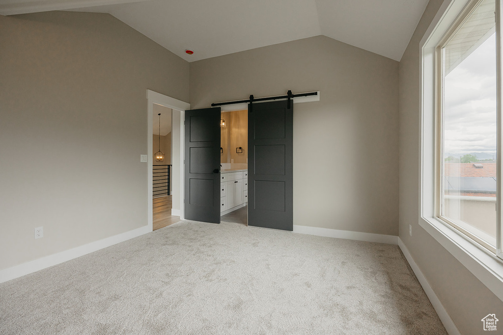 Unfurnished bedroom with vaulted ceiling, light colored carpet, a barn door, and multiple windows