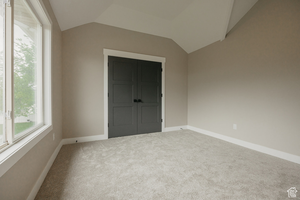 Unfurnished bedroom with lofted ceiling, multiple windows, carpet, and baseboards
