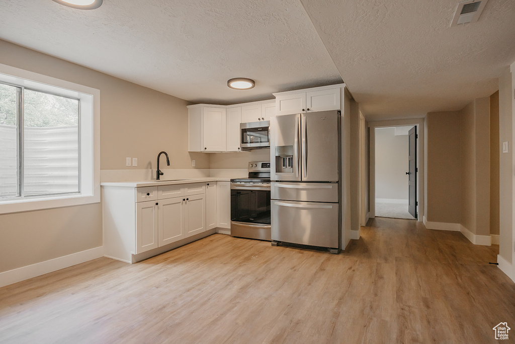 Kitchen with stainless steel appliances, a sink, baseboards, light wood finished floors, and a textured ceiling