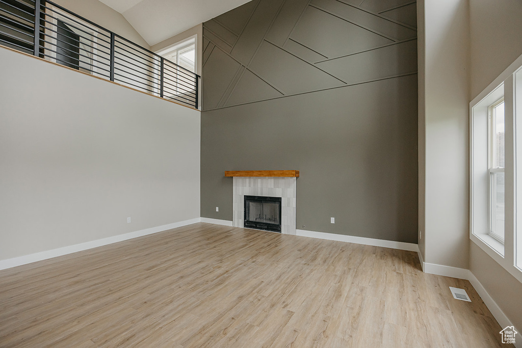 Unfurnished living room with light wood-style flooring, a tile fireplace, baseboards, and high vaulted ceiling