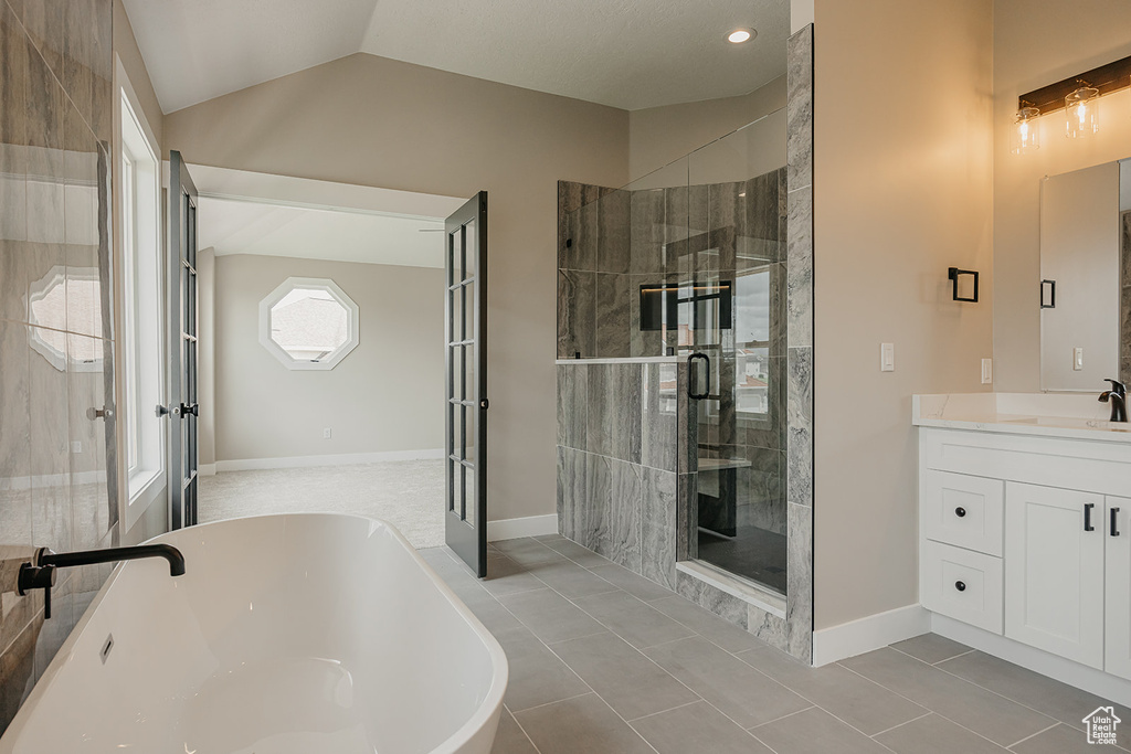 Full bath with a shower stall, a freestanding bath, lofted ceiling, tile patterned floors, and vanity